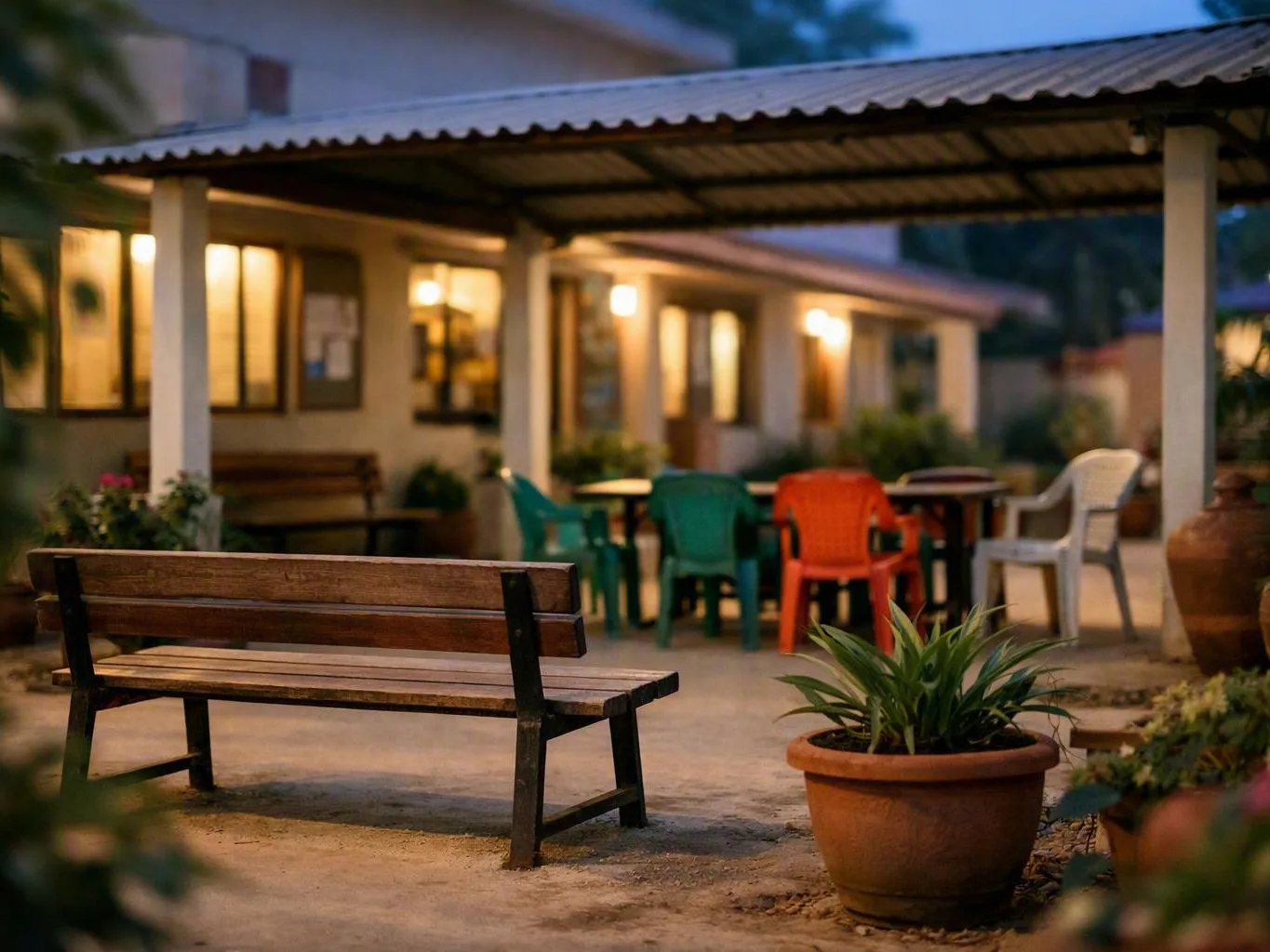 Quiet courtyard with potted plants, colourful chairs, and warmly lit windows at