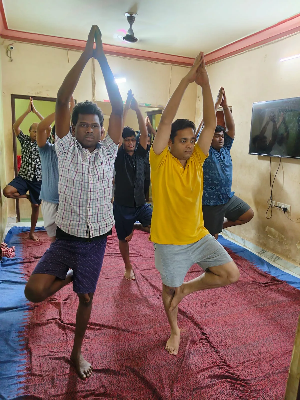 Men practicing tree pose during a yoga class inside a small treatment room
