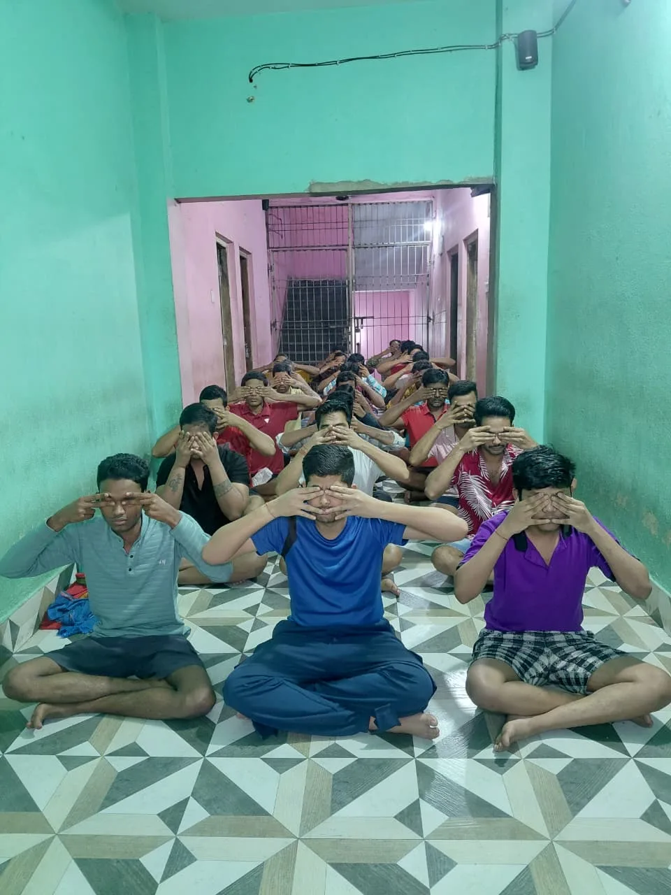 Men covering their eyes together during a guided exercise in a narrow hallway