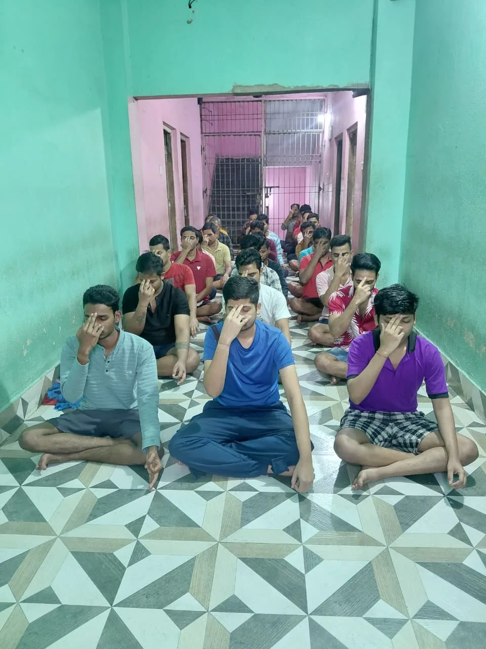 Men sitting cross-legged and holding their noses in a narrow pink corridor