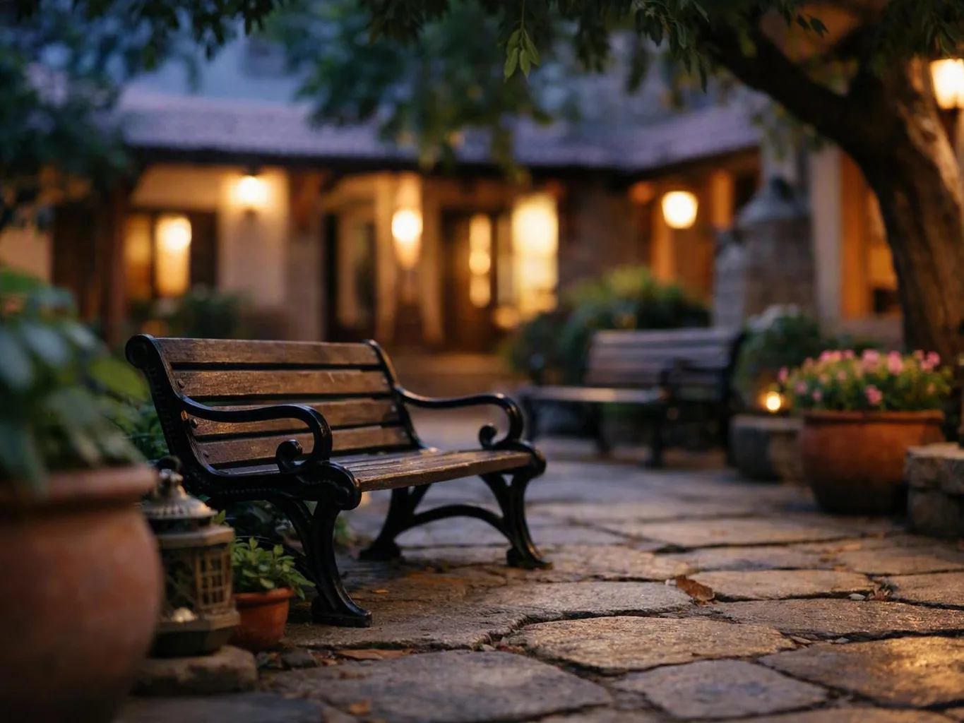 Wooden bench sits on a stone patio outside a warmly lit house at dusk